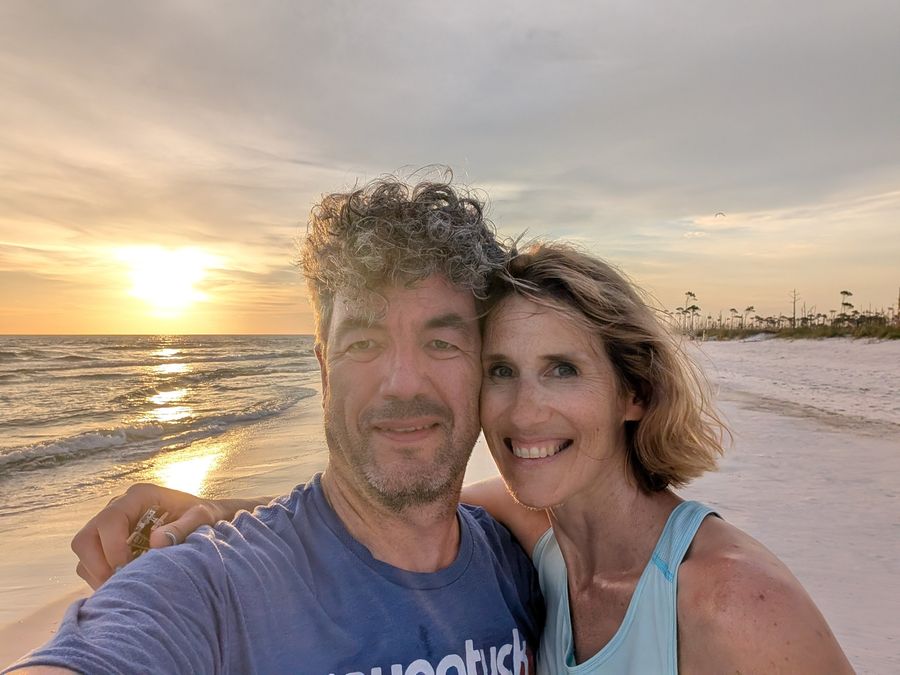 Ken and Lisa close together on the shoreline at Crooked Island Beach as the sun sets over the Gulf